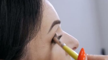 Aynanın önündeki güzel, gösterişli genç kadın özel bir fırçayla yüz ve göz makyajı yapıyor.