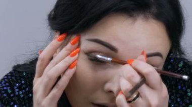 Aynanın önündeki güzel, gösterişli genç kadın özel bir fırçayla yüz ve göz makyajı yapıyor.