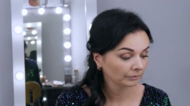 Aynanın önündeki güzel, gösterişli genç kadın özel bir fırçayla yüz ve göz makyajı yapıyor.