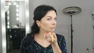 Aynanın önünde duran güzel ve gösterişli genç kadın makyaj ve fondöten ya da özel bir fırçayla kapatıcı sürüyor.