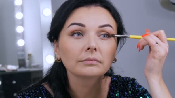 Jovem bela mulher vistosa na frente do espelho aplica maquiagem rosto e olho com uma escova especial — Vídeo de Stock
