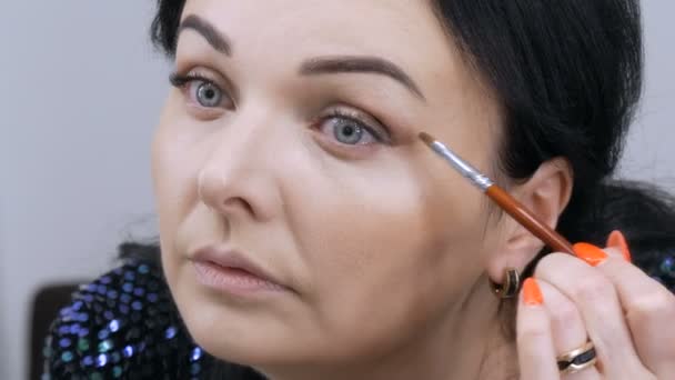 Joven hermosa mujer vistosa delante del espejo se aplica maquillaje de cara y ojos con un cepillo especial — Vídeo de stock