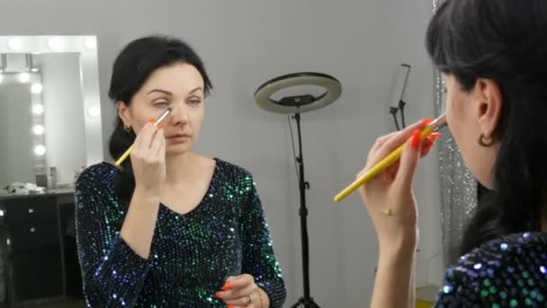 Mladá krásná showy žena v přední části zrcadla aplikuje tvář a oční make-up se speciálním štětcem — Stock video