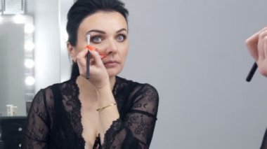 Siyah bir peignoir ve yakası olan güzel bir genç kadın aynanın önünde özel bir fırçayla yüzüne makyaj yapıyor.