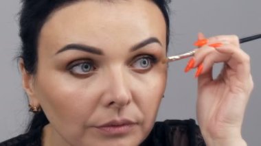 Siyah bir peignoir ve yakası olan güzel bir genç kadın aynanın önünde özel bir fırçayla yüzüne makyaj yapıyor.