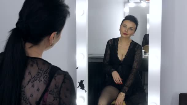 Piękny showowy młoda kobieta z długimi włosami i w czarny peignir i dekolt patrzy na jej odbicie w lustrze. — Wideo stockowe