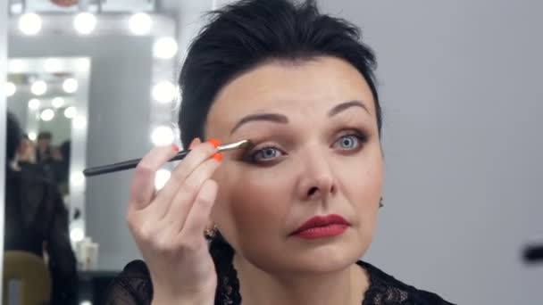 Een mooie spectaculaire jonge vrouw in brengt make-up op haar gezicht met een speciale borstel voor een spiegel — Stockvideo