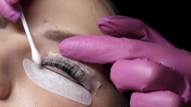 Profesyonel bir güzellik salonunda kirpik kaplama prosedüründen önce genç bir kızın yüzü. Usta kirpik kıvırma işlemi sırasında kirpiklerdeki siyah boyayı özel bir fırçayla yıkar.