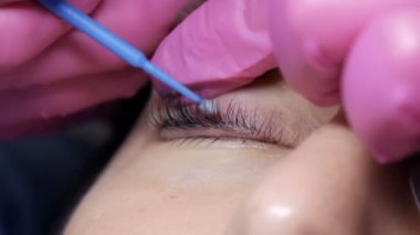 Profesyonel bir güzellik salonunda kirpik kaplama prosedüründen önce genç bir kızın yüzü. Usta kirpik kıvırma işlemi sırasında kirpiklerdeki siyah boyayı özel bir fırçayla yıkar.