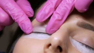 Profesyonel bir güzellik salonunda modern kirpik kaplama prosedürü. Usta kirpik kıvırma işleminden önce özel silikon bigudiler uyguluyor.
