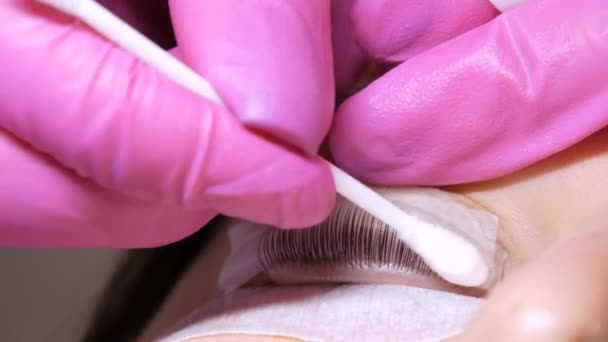 Gezicht van een jong meisje voor een moderne wimper lamineren procedure in een professionele schoonheidssalon. De master wast de speciale lijm af met een wattenstaafje voor de wimperkrulprocedure — Stockvideo