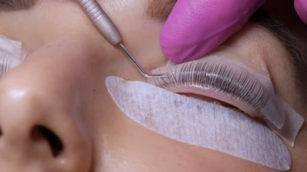 Gesicht eines jungen Mädchens vor einem modernen Wimpernkaschierungsverfahren in einem professionellen Schönheitssalon. Der Meister trägt vor dem Wimpernkräuseln Spezialkleber in rosa Gummihandschuhen auf — Stockvideo