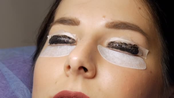 Face of a young girl before a modern eyelash lamination procedure in a professional beauty salon. Master apply black dye to the eyelashes during the eyelash curling procedure with a special brush — Stock Video