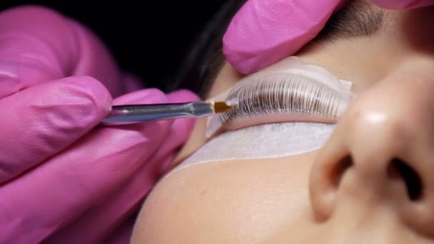 Gezicht van een jong meisje voor een moderne wimper lamineren procedure in een professionele schoonheidssalon. De master brengt een chemische stof aan tijdens de wimper curling procedure met een speciale kwast kluiten omhoog — Stockvideo