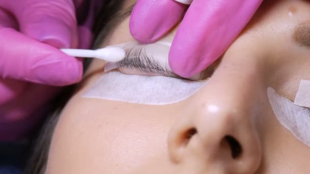 Face of a young girl before a modern eyelash lamination procedure in a professional beauty salon. The master washes off the special glue with a cotton swab before the eyelash curling procedure — Stock Video