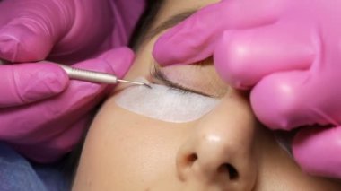 Profesyonel bir güzellik salonunda modern kirpik kaplama prosedürü. Usta kirpikleri özel yapışkan bantlara takar. Kirpik kıvırma işleminden önce özel bir iğne kullanır.