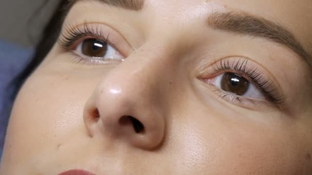 Het gezicht van een jong meisje voor een moderne wimper lamineren procedure in een professionele schoonheidssalon voor de wimper curling procedure. Portret van een vrouw zonder make-up met donkere lippenstift — Stockvideo