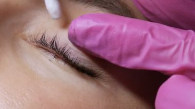 Profesyonel bir güzellik salonunda kirpik kaplama prosedüründen önce genç bir kızın yüzü. Usta kirpik kıvırma işlemi sırasında kirpiklerdeki siyah boyayı özel bir fırçayla yıkar.