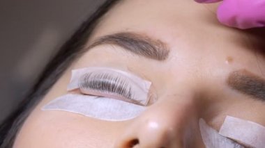 Profesyonel bir güzellik salonunda modern kirpik temizleme prosedüründen önce genç bir kızın yüzü. Usta, kirpik kıvırma işleminden önce özel yapıştırıcıyı pamukla yıkar.