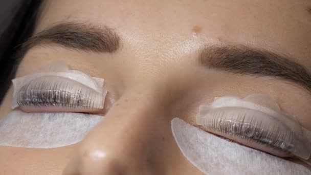 Gesicht eines jungen Mädchens vor einem modernen Wimpernkaschierungsverfahren in einem professionellen Schönheitssalon. Beim Wimpernkräuseln trägt der Meister eine Chemikalie mit einer speziellen Bürste auf. — Stockvideo
