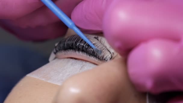 Faccia di ragazza prima di procedura di laminazione di ciglio in un salone di bellezza professionale. Il maestro lava via la vernice nera sulle ciglia durante la procedura di arricciatura delle ciglia con un pennello speciale — Video Stock