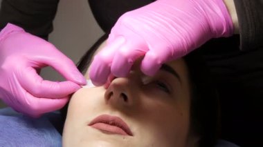 Profesyonel bir güzellik salonunda modern kirpik kaplama prosedürü. Usta kirpik kıvırma işleminden önce gözlere özel yapışkan bantlar yapıştırır.