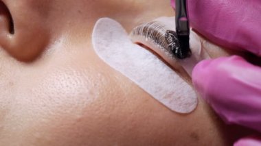 Profesyonel bir güzellik salonunda kirpik temizleme işlemi yapan genç bir kızın yüzü. Usta kirpik kıvırma işlemi sırasında kirpiklere özel bir fırçayla siyah boya sür