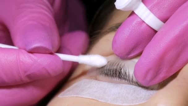 Gesicht eines jungen Mädchens vor einem modernen Wimpernkaschierungsverfahren in einem professionellen Schönheitssalon. Der Meister wäscht den Spezialkleber vor dem Wimpernkräuseln mit einem Wattestäbchen ab — Stockvideo