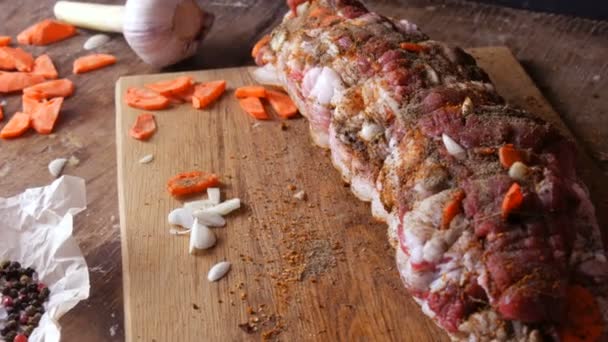 Pezzo fresco succoso di carne cruda carne di maiale bistecca o pancetta con condimenti di pepe, aglio, carote in stile rustico riavvolto con filetti di cottura in forno salati e speziati, guarniti su fondo di legno — Video Stock