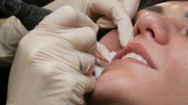 Kozmetoloji kliniğindeki dudak rengini düzelten özel renk pigmentli mikro patenli dudak dövmesi. Eller, dövme makinesiyle dudaklara pigment makyajı uygulayarak kalıcı makyaj yapar.