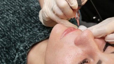 Kozmetoloji kliniğindeki dudak rengini düzelten özel renk pigmentli mikro patenli dudak dövmesi. Eller, dövme makinesiyle dudaklara pigment makyajı uygulayarak kalıcı makyaj yapar.