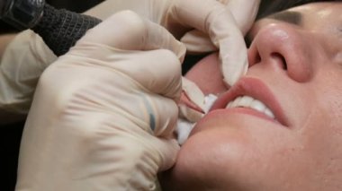 Kozmetoloji kliniğindeki dudak rengini düzelten özel renk pigmentli mikro patenli dudak dövmesi. Eller, dövme makinesiyle dudaklara pigment makyajı uygulayarak kalıcı makyaj yapar.