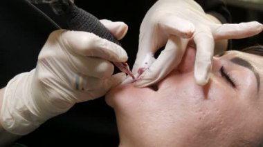 Kozmetoloji kliniğindeki dudak rengini düzelten özel renk pigmentli mikro patenli dudak dövmesi. Eller, dövme makinesiyle dudaklara pigment makyajı uygulayarak kalıcı makyaj yapar.