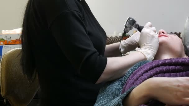 Microblading τατουάζ με ειδική χρωστική ουσία χρωματισμό που διορθώνει το χρώμα των χειλιών στην κλινική κοσμετολογίας. Beautician κάνει μόνιμη διαδικασία μακιγιάζ χείλη εφαρμογή μακιγιάζ χρωστική στα χείλη με μηχανή τατουάζ — Αρχείο Βίντεο