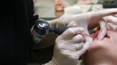 Kozmetoloji kliniğindeki dudak rengini düzelten özel renk pigmentli mikro patenli dudak dövmesi. Eller, dövme makinesiyle dudaklara pigment makyajı uygulayarak kalıcı makyaj yapar.