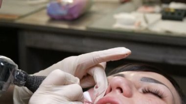 Kozmetoloji kliniğindeki dudak rengini düzelten özel renk pigmentli mikro patenli dudak dövmesi. Eller, dövme makinesiyle dudaklara pigment makyajı uygulayarak kalıcı makyaj yapar.