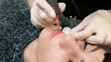 Kozmetoloji kliniğindeki dudak rengini düzelten özel renk pigmentli mikro patenli dudak dövmesi. Eller, dövme makinesiyle dudaklara pigment makyajı uygulayarak kalıcı makyaj yapar.