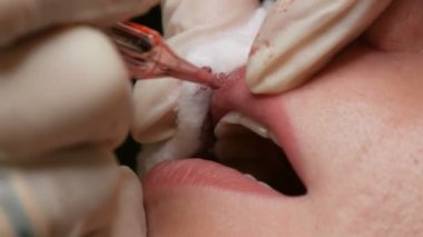 Kozmetoloji kliniğindeki dudak rengini düzelten özel renk pigmentli mikro patenli dudak dövmesi. Eller, dövme makinesiyle dudaklara pigment makyajı uygulayarak kalıcı makyaj yapar.