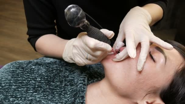 Микролезвие татуировка губы со специальным красящим пигментом, который корректирует цвет губ в косметологической клинике. Руки делает постоянный макияж губы процедура нанесения пигмента макияж на губы с татуировкой машины — стоковое видео