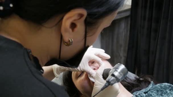 Tatouage Microblading avec un pigment colorant spécial qui corrige la couleur des lèvres dans la clinique de cosmétologie. L'esthéticienne fait une procédure permanente de maquillage des lèvres en appliquant du maquillage pigmenté sur les lèvres avec machine à tatouer — Video