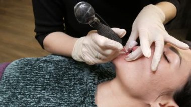Kozmetoloji kliniğindeki dudak rengini düzelten özel renk pigmentli mikro patenli dudak dövmesi. Eller, dövme makinesiyle dudaklara pigment makyajı uygulayarak kalıcı makyaj yapar.