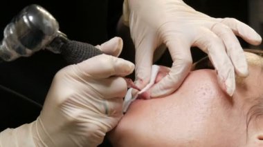 Kozmetoloji kliniğindeki dudak rengini düzelten özel renk pigmentli mikro patenli dudak dövmesi. Eller, dövme makinesiyle dudaklara pigment makyajı uygulayarak kalıcı makyaj yapar.