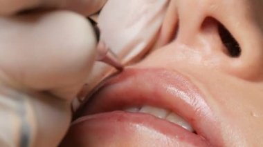 Kozmetik uzmanı, dövme makinesi pembe pigmenti kullanarak dudaklarını mikro patinaj yaptırıyor. Kadın dudaklarına pigment makyajı yapan bir güzellik uzmanı. Güzellik salonunda güzellik endüstrisi kavramı