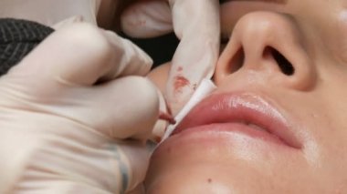 Kozmetik uzmanı, dövme makinesi pembe pigmenti kullanarak dudaklarını mikro patinaj yaptırıyor. Kadın dudaklarına pigment makyajı yapan bir güzellik uzmanı. Güzellik salonunda güzellik endüstrisi kavramı