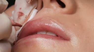 Kozmetik uzmanı, dövme makinesi pembe pigmenti kullanarak dudaklarını mikro patinaj yaptırıyor. Kadın dudaklarına pigment makyajı yapan bir güzellik uzmanı. Güzellik salonunda güzellik endüstrisi kavramı