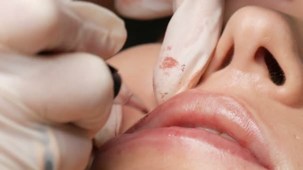 Cosmetologue faire des lèvres microblading procédure permanente à l'aide d'une machine à tatouer pigment rose. Esthéticienne appliquant du maquillage pigmentaire sur les lèvres des femmes. Concept de l'industrie de la beauté dans le salon d'esthéticienne close up — Video