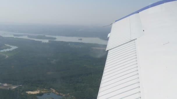 在白色机翼的背景下，从一架小型私人客机的窗口观看。房屋、绿林、田野、湖泊、河流尽收眼底 — 图库视频影像