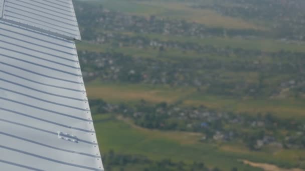 飞机的白色侧翼，俯瞰着绿林、小木屋和城镇的顶部。旅行概念 — 图库视频影像