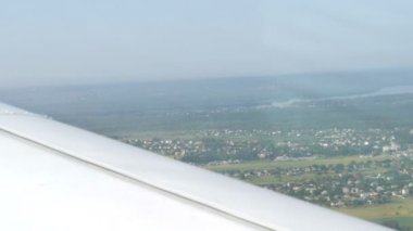 Küçük bir yolcu uçağının penceresinden beyaz bir kanadın arka planına bakın. Ev manzarası, yeşil ormanlar, tarlalar, göller, nehirler