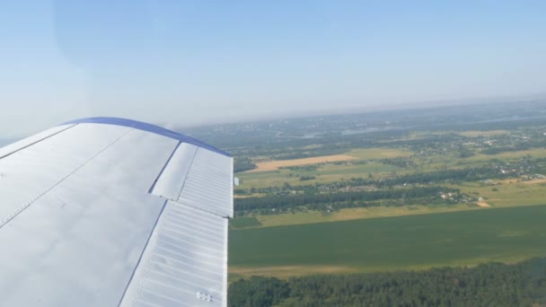 De witte vleugel van een passagiersvliegtuig tegen het bovenaanzicht van groene bossen en kleine huizen en steden. Reisconcept — Stockvideo